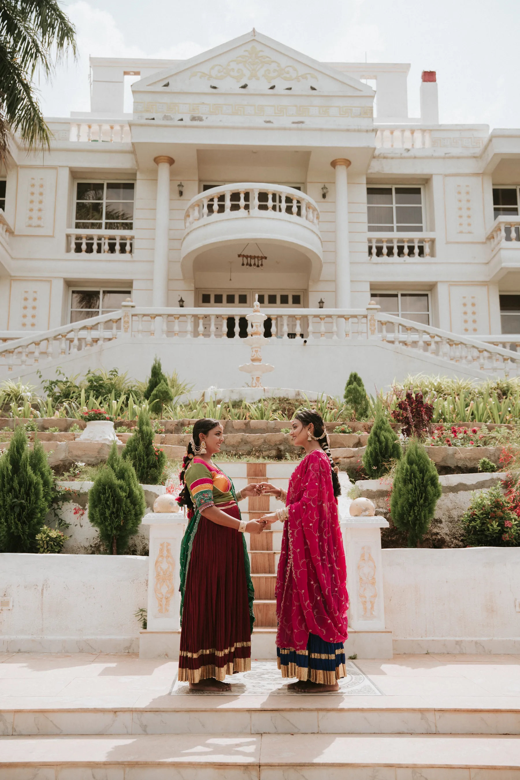 Two women in colourful traditional outfits outside a white heritage-style building